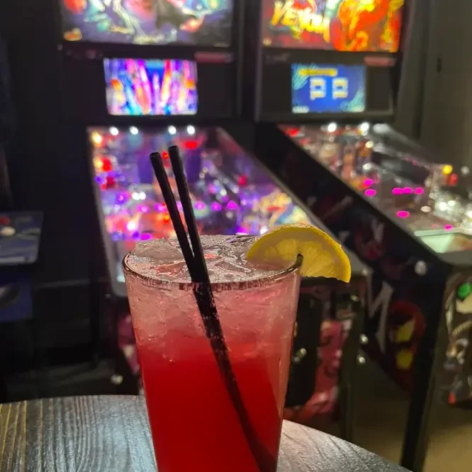 An Arcade 11 drink beside the pinball games